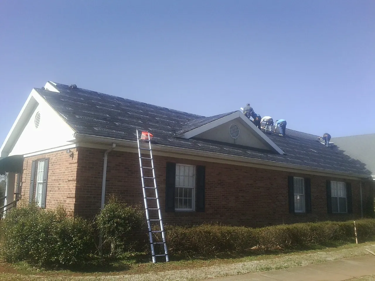 Crew tearing shingles off a brick ranch roof with a ladder set — Metal Roof Repair work by our crew in Stanton