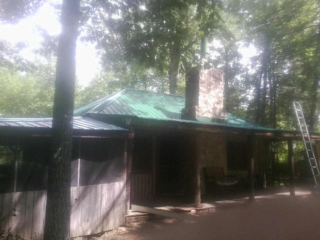 Green metal roof and stone chimney above a log cabin porch in Stanton